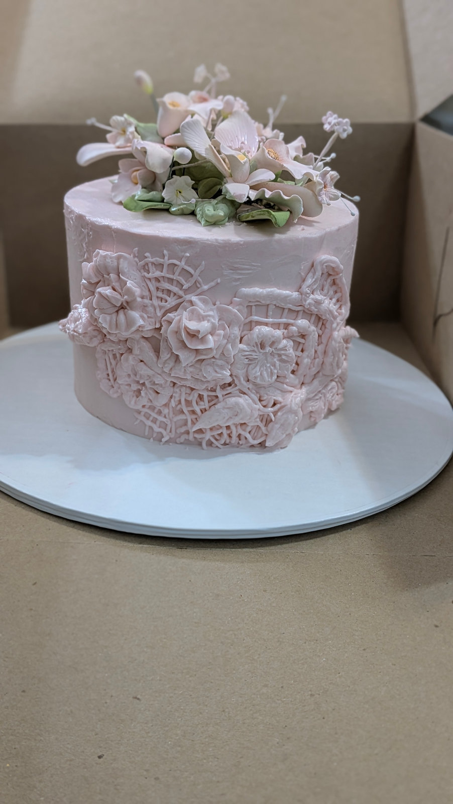 Pale pink cake with piped lace detail and a cluster of sugar flowers on top