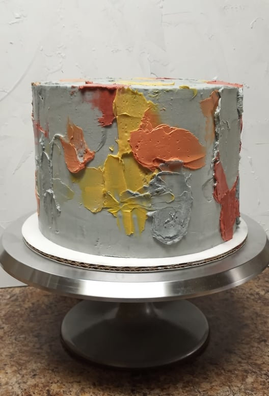 Cement-effect cake with grey, orange and yellow brushstrokes on a cake stand
