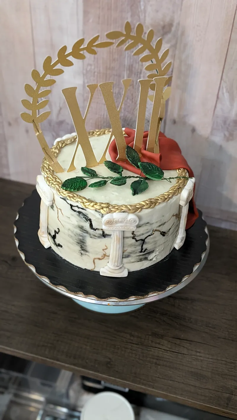 Cracked-marble effect cake with a red drape, green leaves and a gold laurel and Roman numeral topper