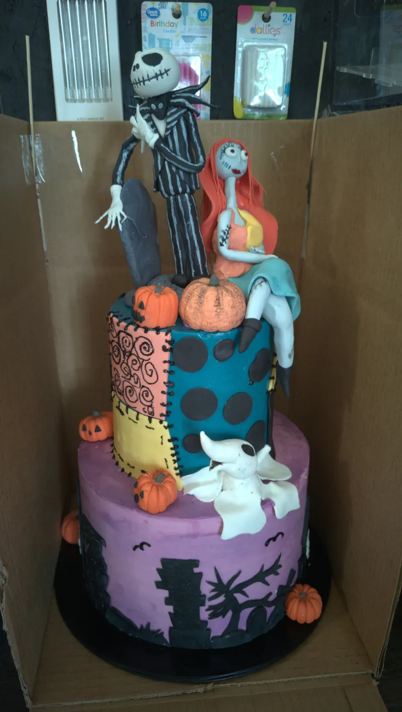 Tall tiered Halloween cake with sculpted Jack Skellington and Sally figures, pumpkins and a purple graveyard tier