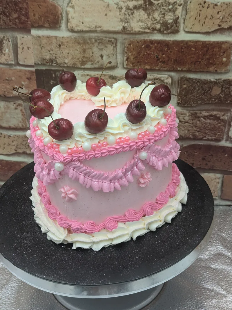 Pink vintage-piped cake topped with dark cherries