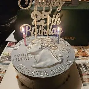 Birthday cake decorated as a giant silver quarter with a gold 25th Birthday topper and lit candles