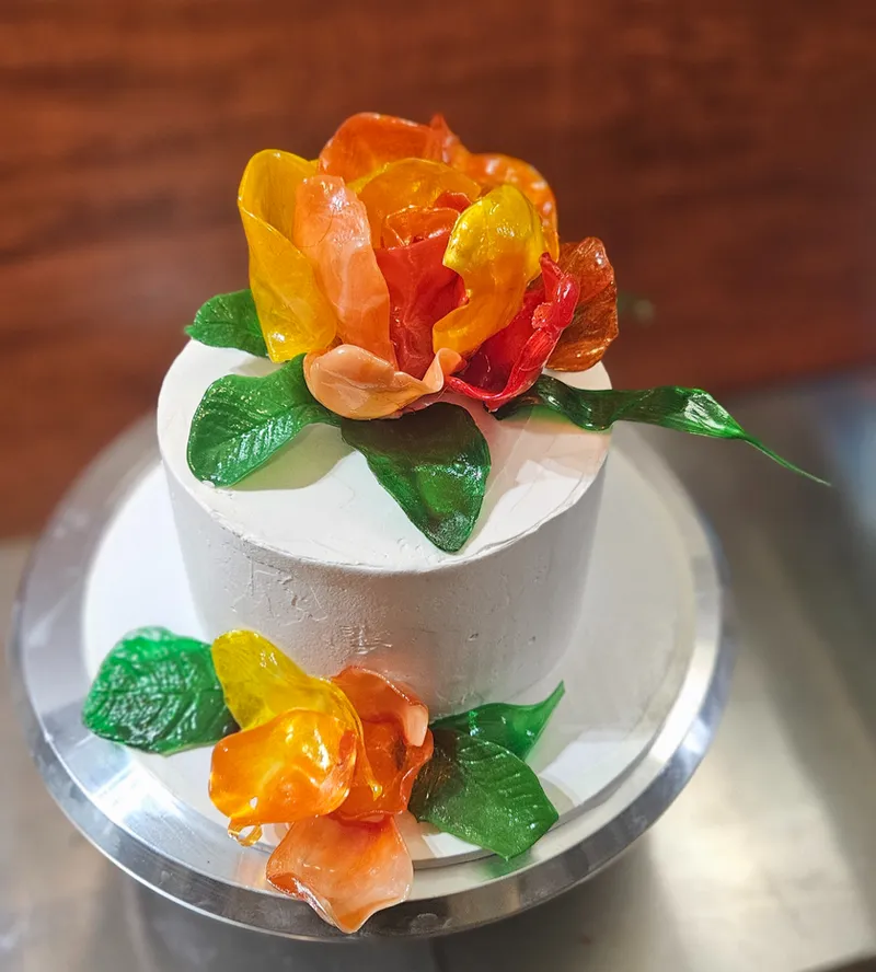 White buttercream celebration cake topped with orange and red pulled and blown sugar flowers and leaves