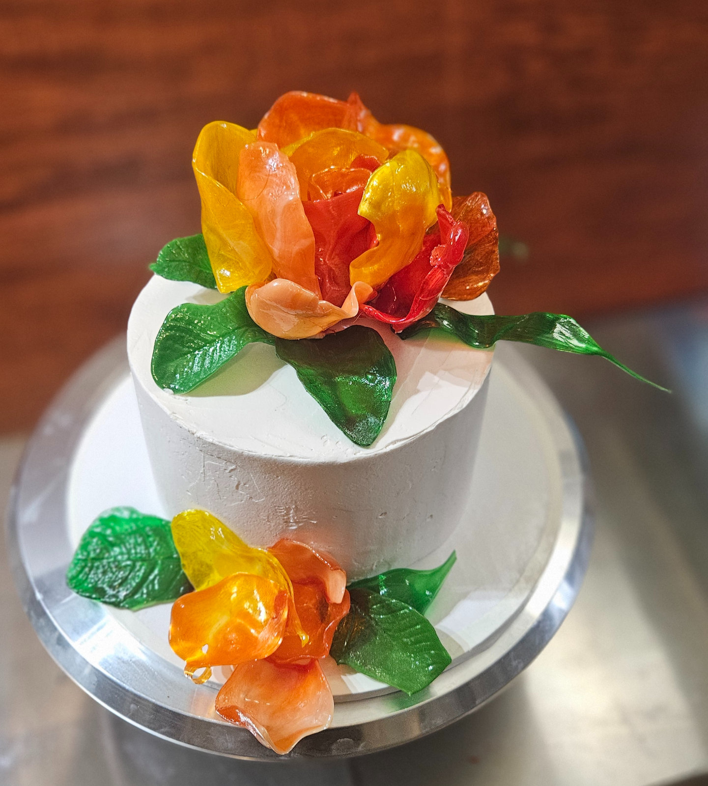 White buttercream celebration cake topped with orange and red pulled and blown sugar flowers and leaves