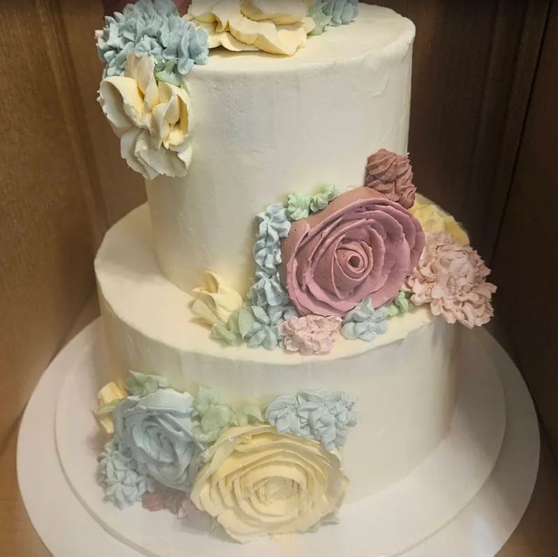 Two-tier ivory buttercream cake decorated with piped roses in blush, butter yellow and sage