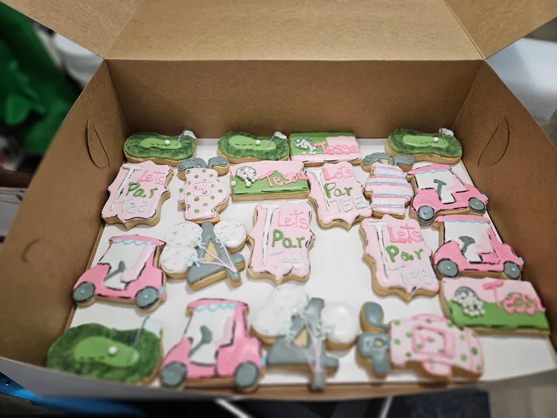 Pink and green golf-themed cookies with golf carts and Par plaques in a bakery box