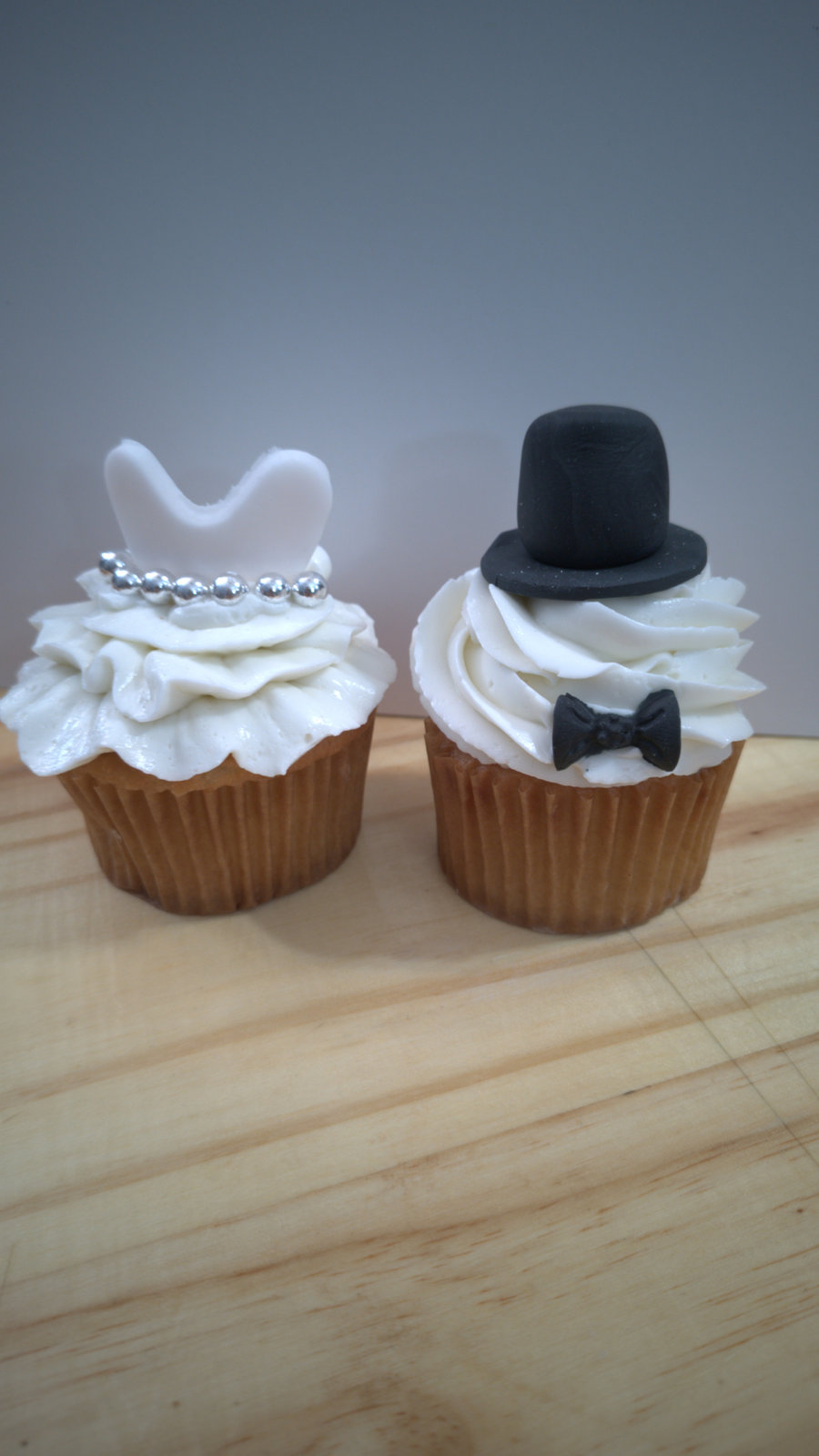 Two wedding cupcakes, one with a white dress and one with a black top hat and bow tie