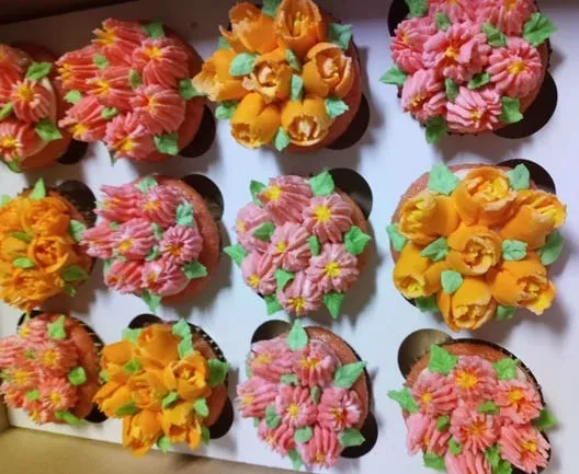 Cupcakes piped with pink and orange buttercream flowers and green leaves