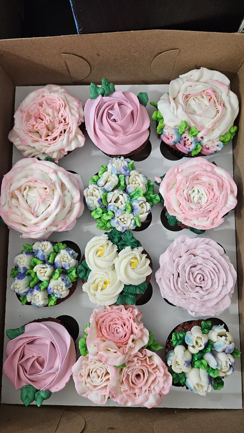 A dozen cupcakes piped with pastel pink and white roses and blossoms