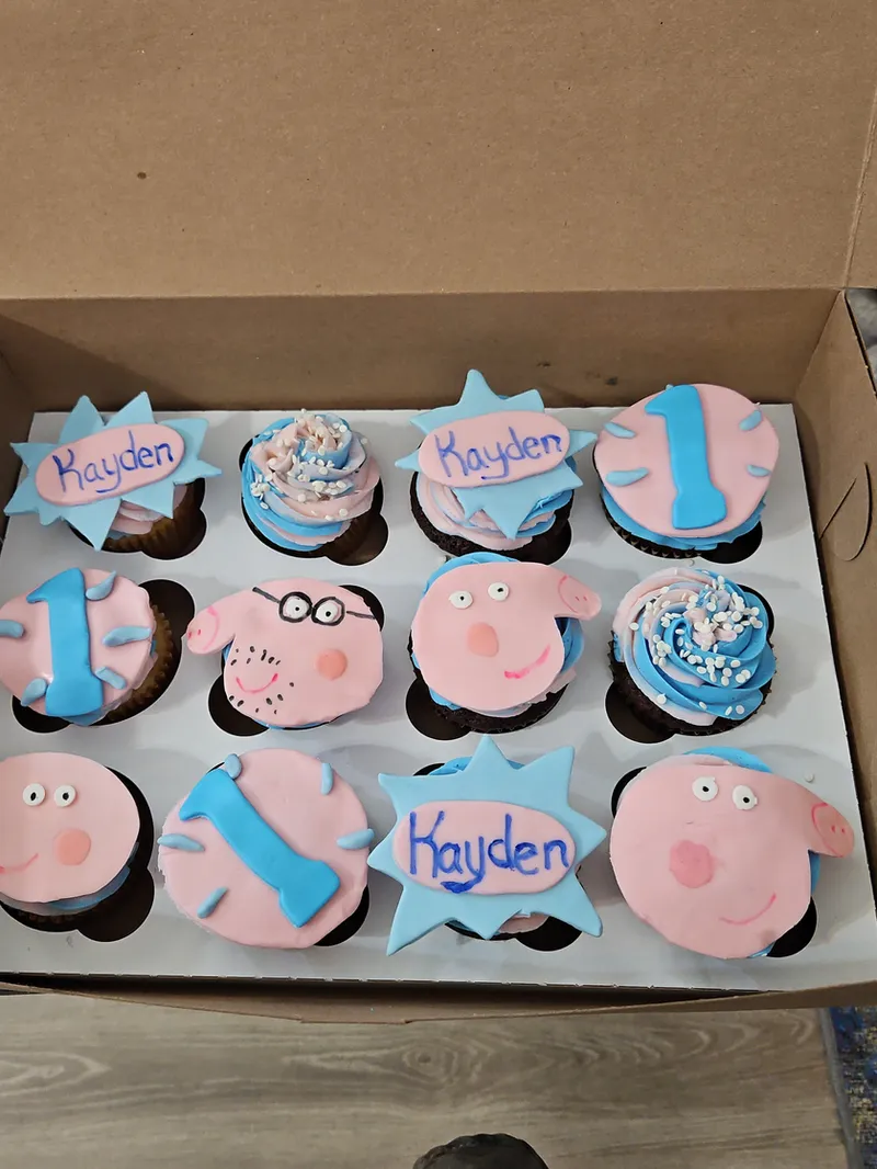 First-birthday cupcakes with pink pig faces, blue number ones and a name