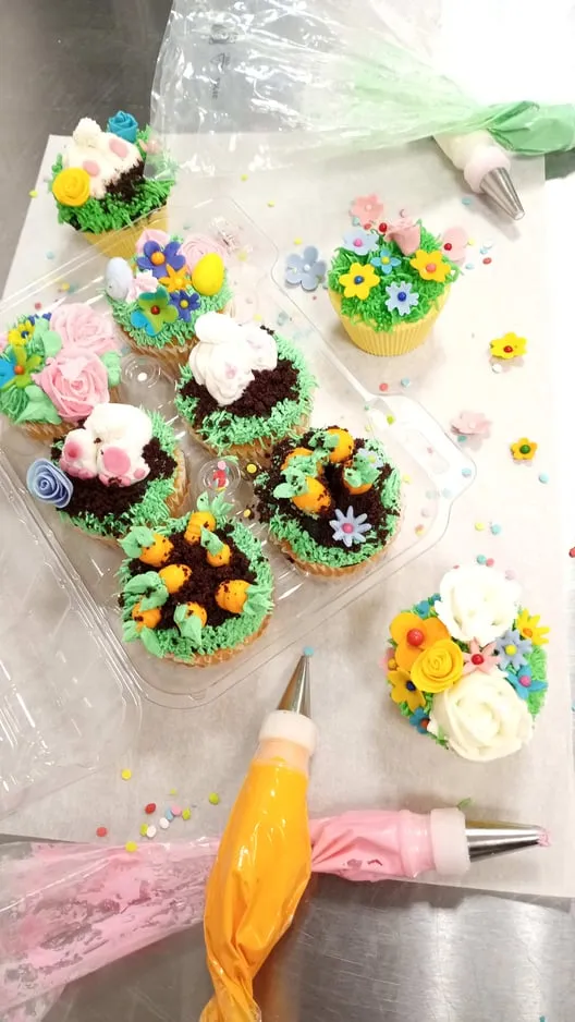 Spring cupcakes with piped grass and small flowers beside a filled piping bag